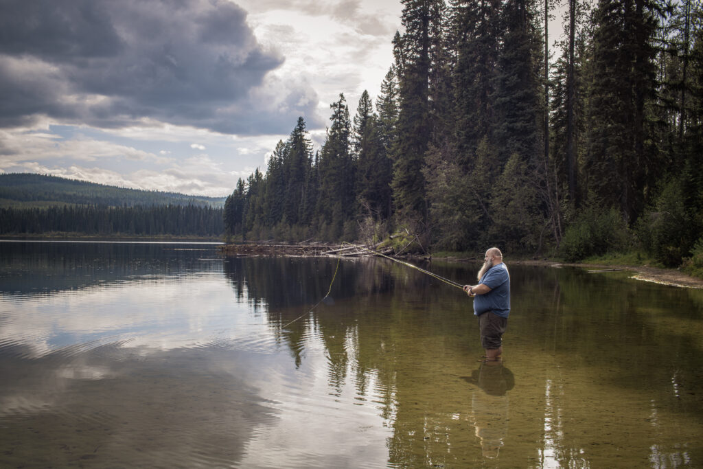 Angler casting a fishing line from the shoreline at Nancy Greene Lake near Rossland BC.