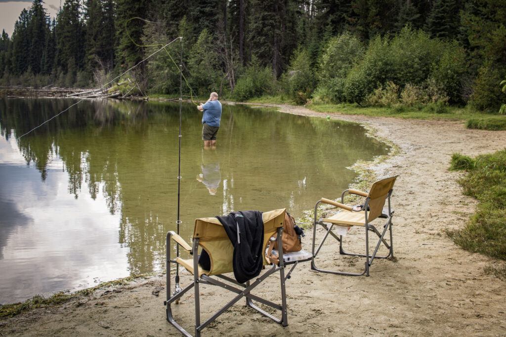 Angler casting a fishing line from the shoreline at Nancy Greene Lake near Rossland BC.