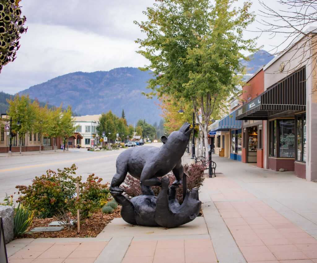 Downtown Rossland in summer with flower baskets, public art, and outdoor seating lining the sidewalks of Columbia Avenue.